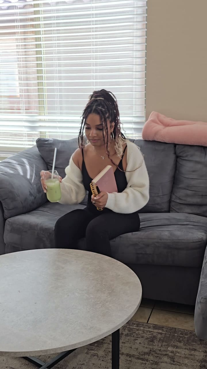 Layla on a grey couch holding a matcha drink and a pink notebook