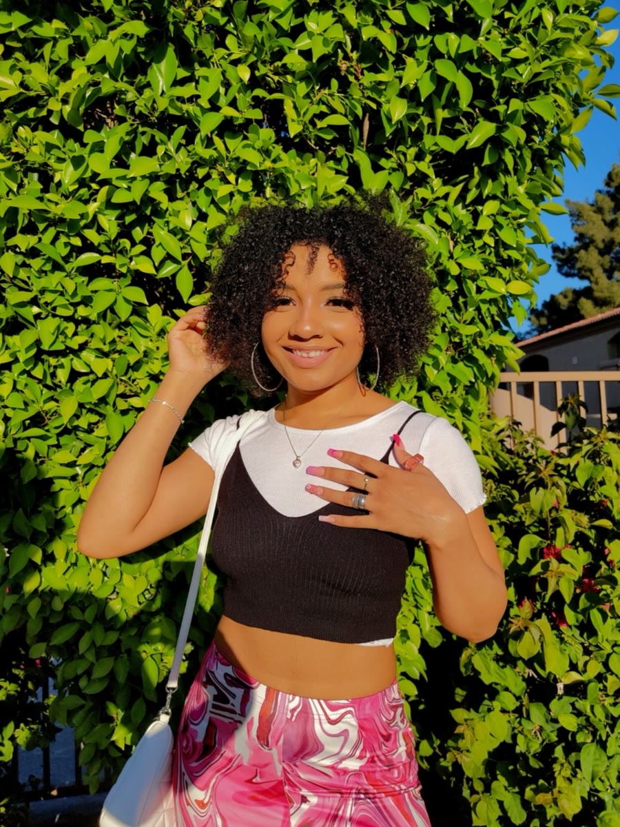 Layla smiling outdoors in front of green hedges